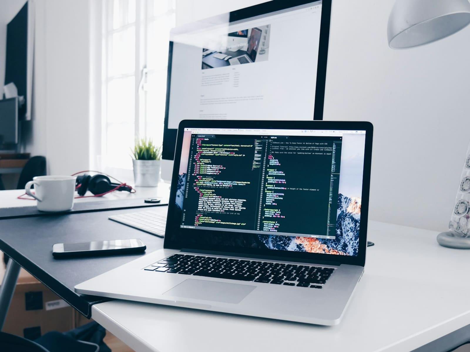 A laptop showing lines of code on a desk beside a coffee cup