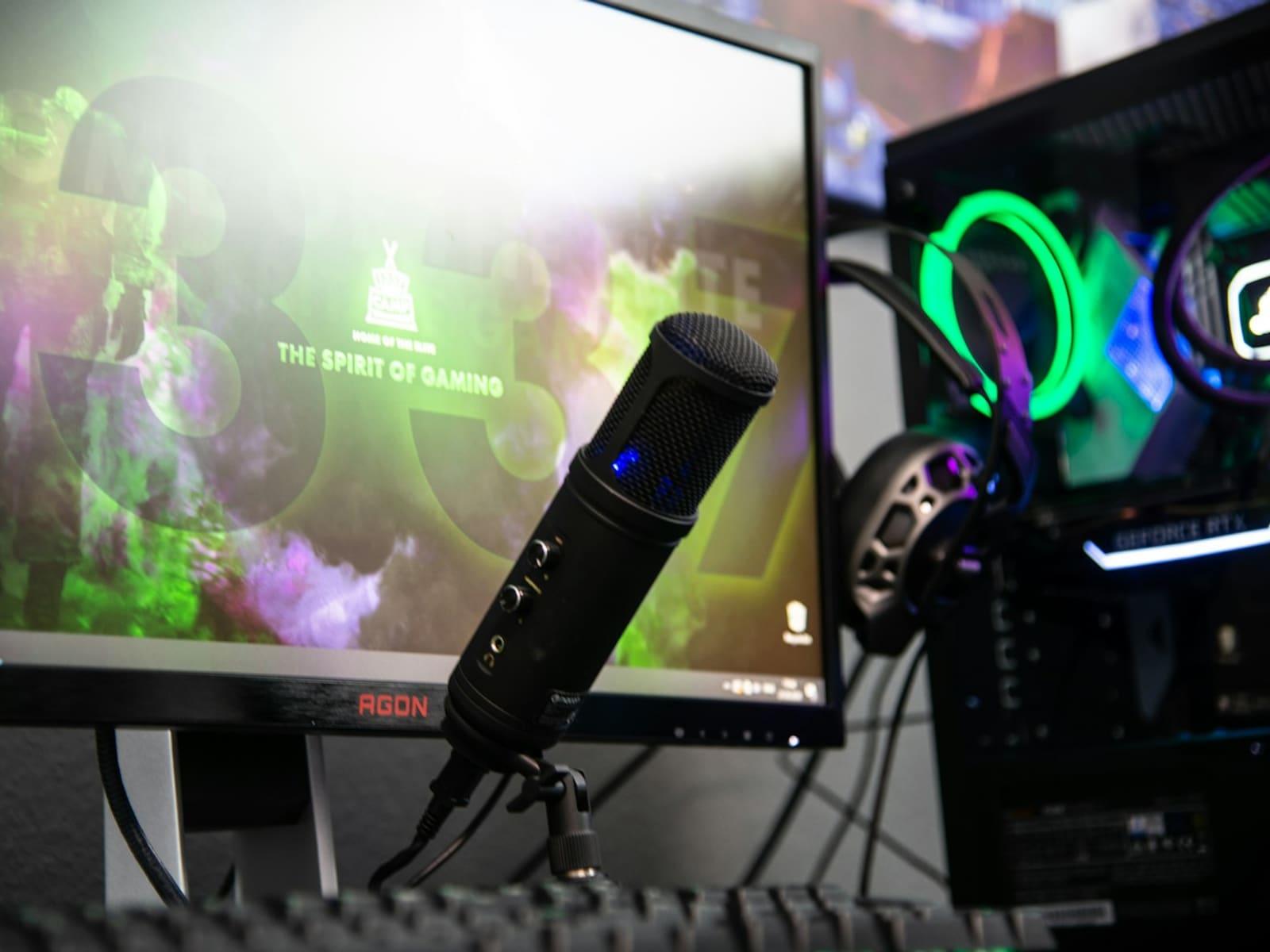 A condenser microphone on an arm beside a monitor and gaming headset