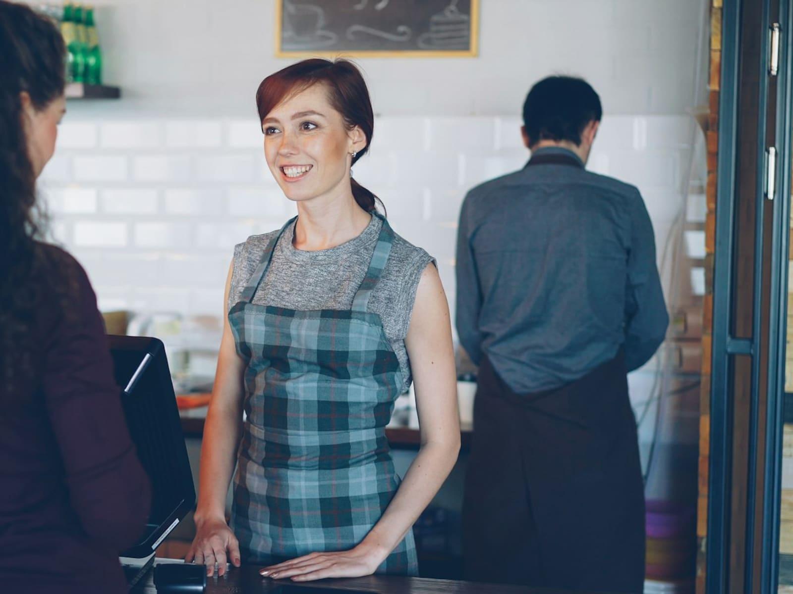 A smiling barista greeting a customer at a cafe counter