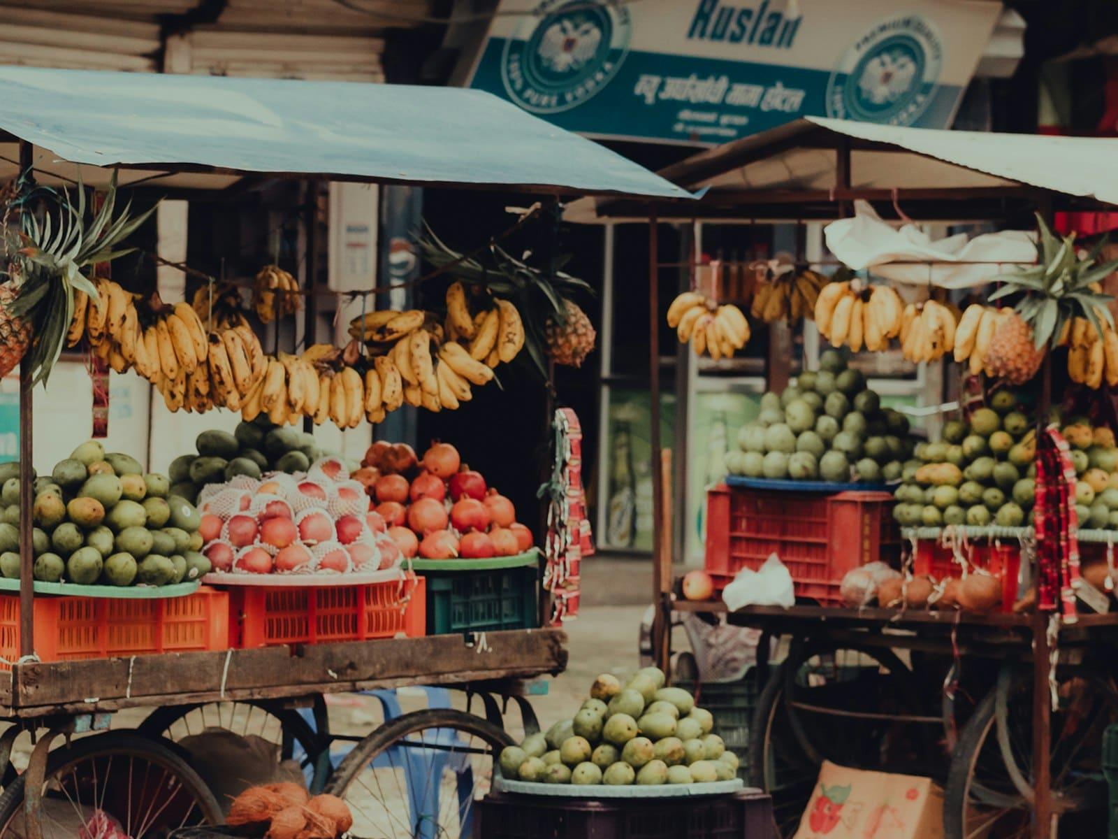 A colourful fruit stall in a street market with bananas hanging above